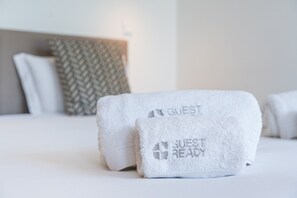 Een keurig opgemaakt bed met twee handdoeken, waarvan één met de tekst 'GUEST' en de ander 'GUEST READY'.