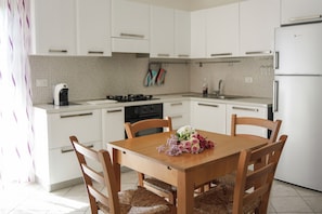 Una cuina moderna amb armaris blancs, una taula de dinar de fusta, cadires de vimet i un ram de flors.
