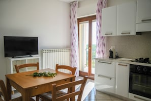 Una cuina moderna amb armaris blancs, forn de pared i zona menjador amb taula i caires de fusta.