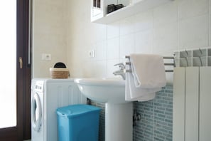 Un baño con lavadora, lavamanos y un perchero para toallas.