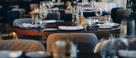 Un ambiente de restaurante con mesas redondas, sillas y copas de vino vacías.