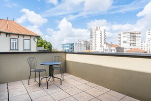 A balcony with two chairs and a table, overlooking a cityscape with modern buildings and a clear sky. - GuestReady - PoetikBlue - Room 7 (Porto)