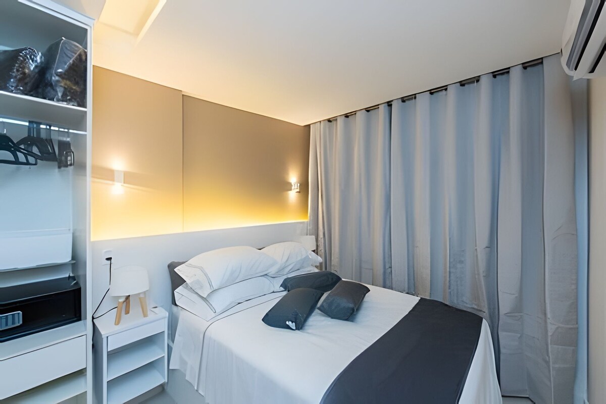 Una habitación de hotel con cama, mesita de noche, lámpara y armario.