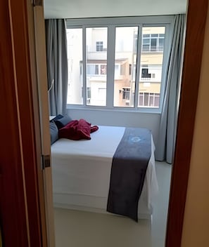 Una habitación de hotel con cama, cortinas y vista a edificios.