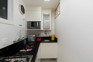 Una cocina compacta con estufa a gas, cafetera, microondas y pileta.