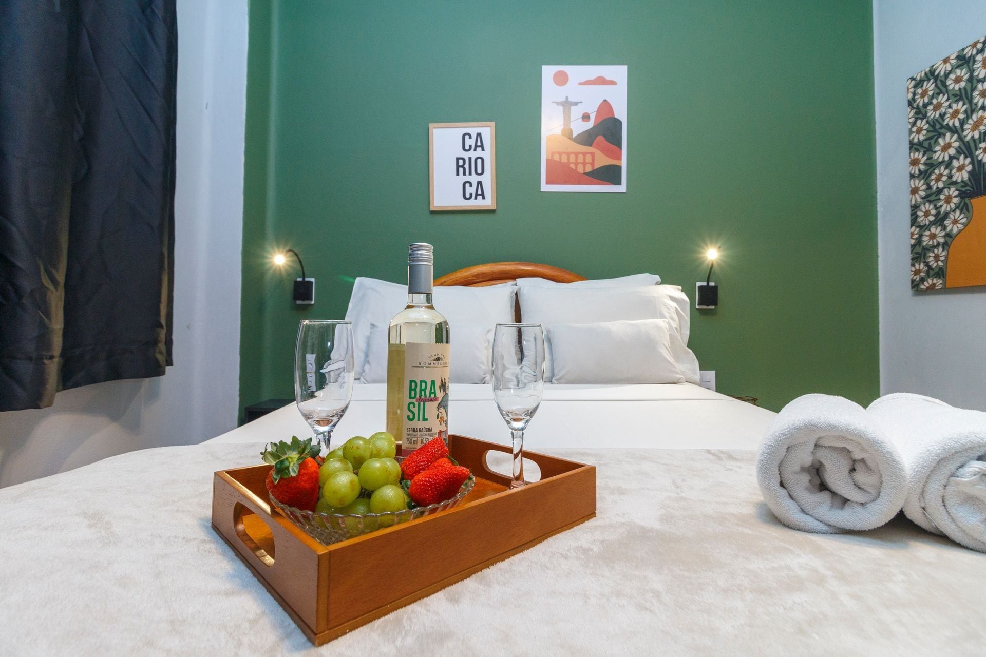 Habitación de hotel con una cama, una bandeja de fruta, una botella de licor y un cuadro en la pared.