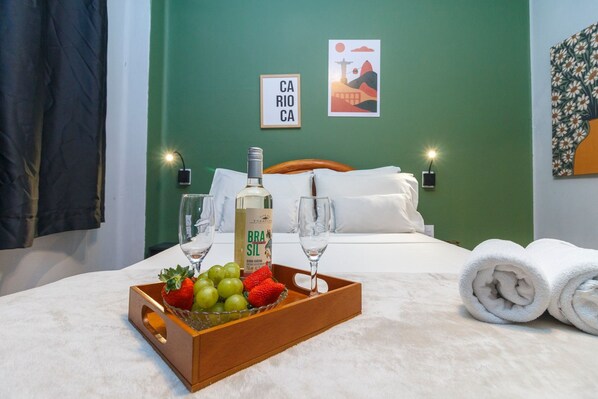 A hotel room with a bed, a tray of fruit, a bottle of alcohol, and a painting on the wall. - BR668 (Rio de Janeiro)