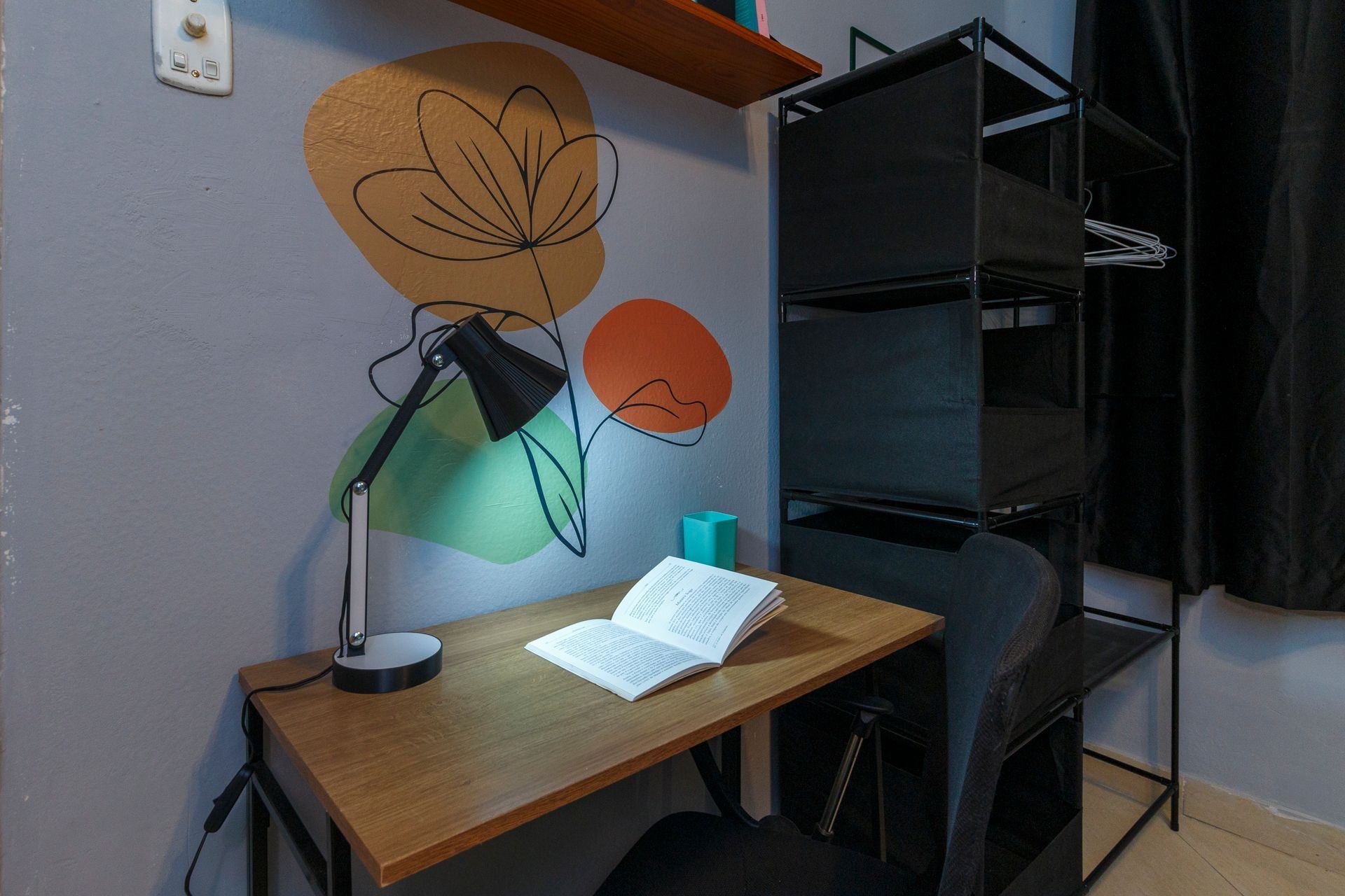 Ein Arbeitsplatz mit Schreibtisch, Lampe, Buch und Wandbild.