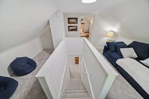 A staircase leading to a bedroom with a bed, a blue sofa, and a lamp. - Hot Tub + Fire Pit | Steelhead Fishing | Sleeps 6 (Erie)
