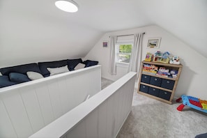 Een kinderkamer met een stapelbed, een opbergmeubel voor speelgoed en een raam met gordijnen.