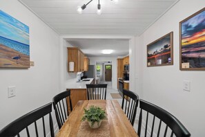 A dining area with a wooden table and chairs, a potted plant, and artwork on the walls. - Hot Tub + Fire Pit | Steelhead Fishing | Sleeps 6 (Erie)