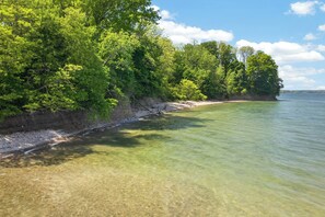 A clear lake with a sandy shore and dense green foliage along the edge. - Hot Tub + Fire Pit | Steelhead Fishing | Sleeps 6 (Erie)