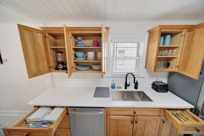 A kitchen with wooden cabinets, a white countertop, a built-in dishwasher, and a window with blinds. - Hot Tub + Fire Pit | Steelhead Fishing | Sleeps 6 (Erie)