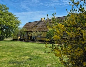Ein traditionelles Haus mit einem Strohdach, umgeben von einem gepflegten Rasen und blühenden Bäumen.