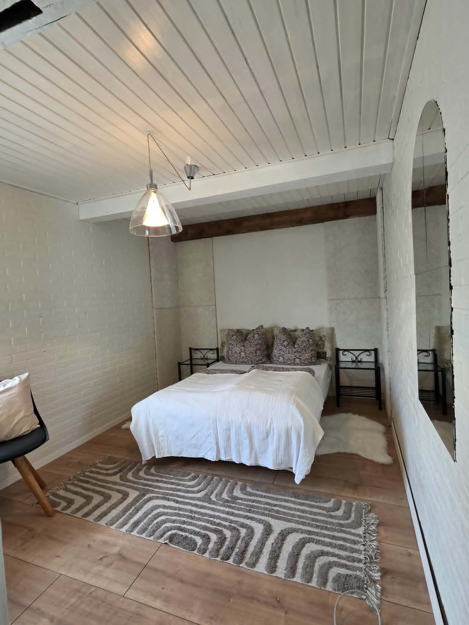 Une chambre à coucher comprenant un lit, une table de chevet, une chaise, un tapis à motifs et un grand miroir.