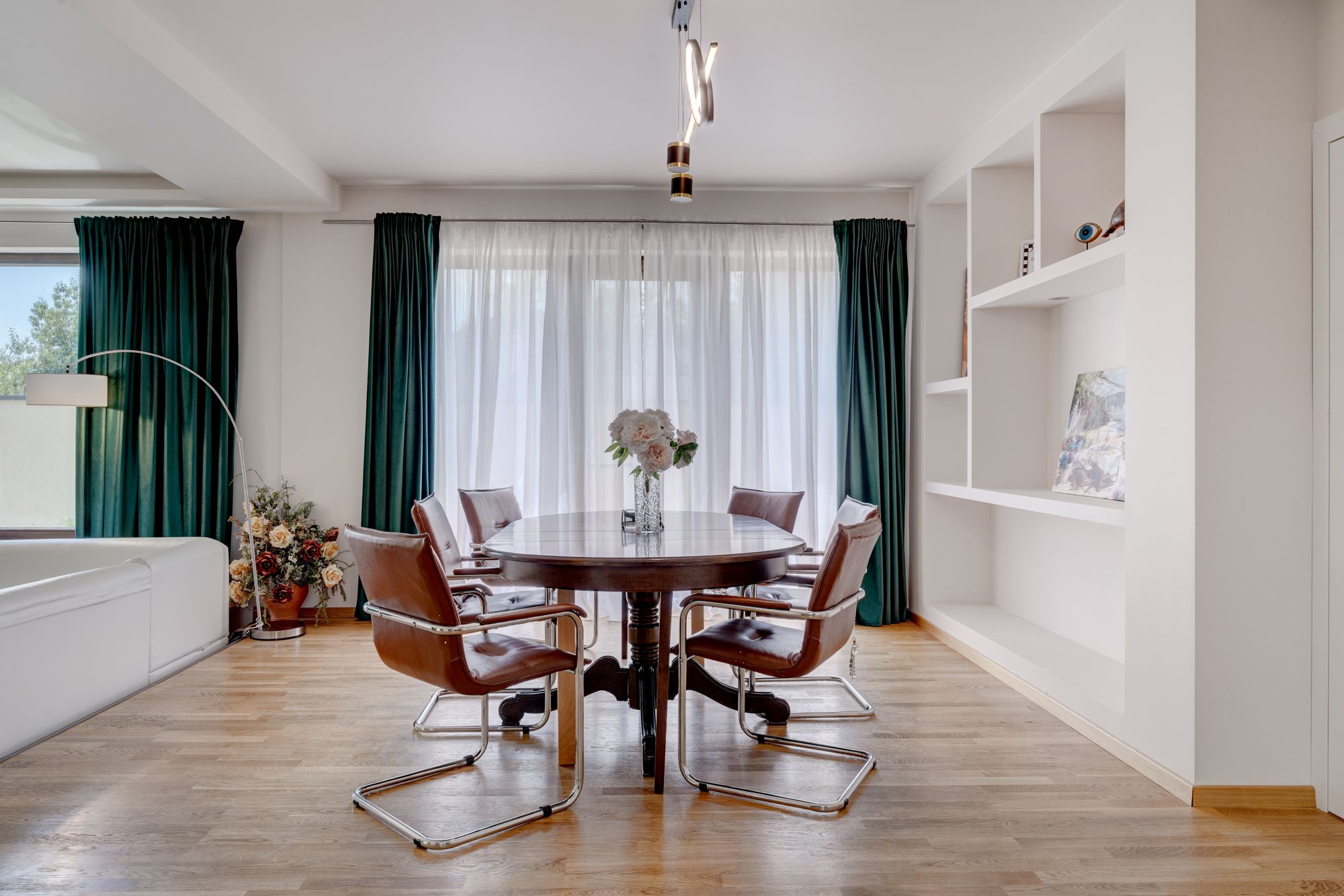 A modern dining room with a round table, six chairs, and a vase of flowers.