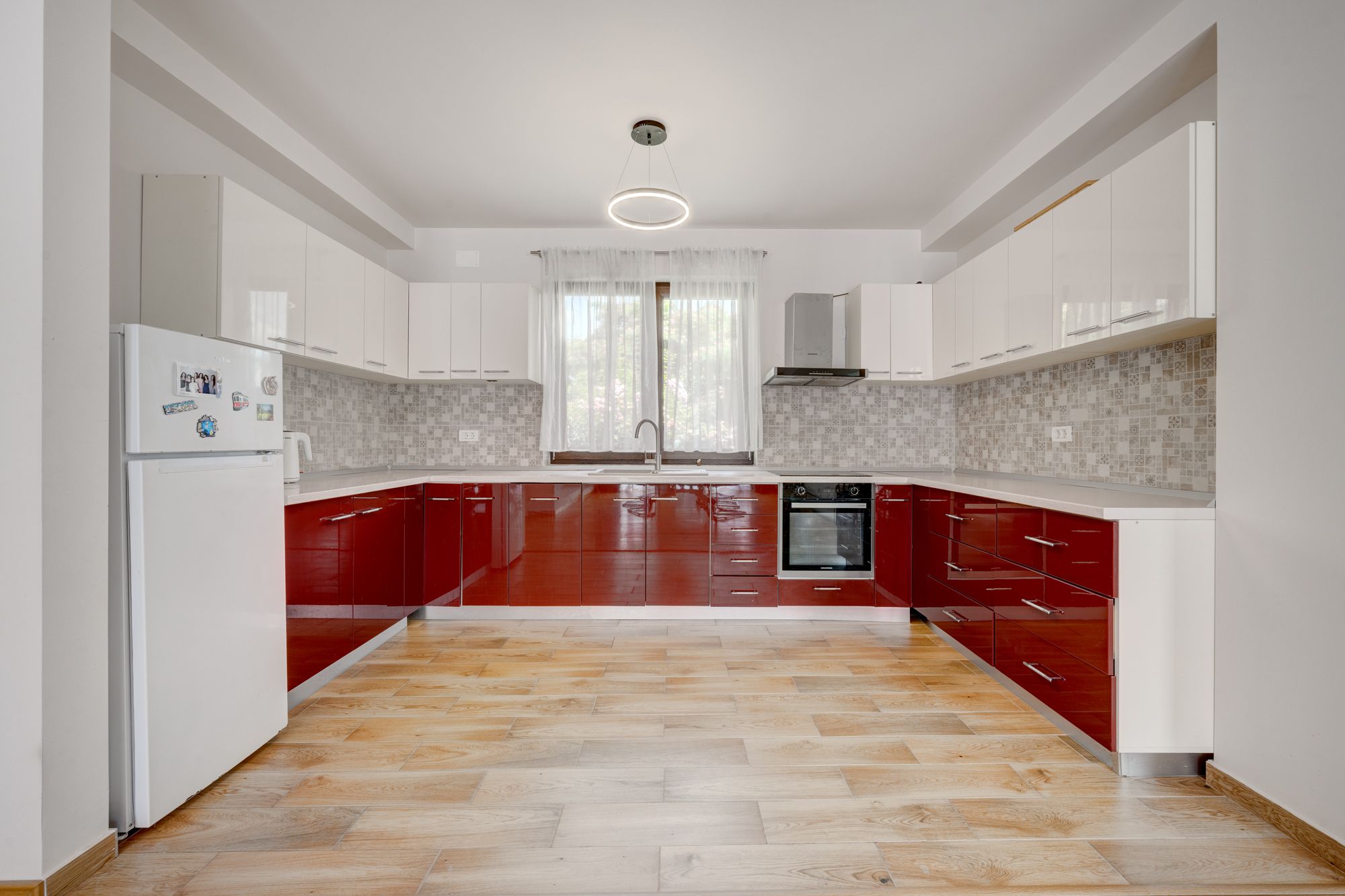 A modern kitchen with white and red cabinetry, a herringbone-patterned floor, and a built-in oven.