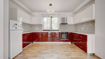 A modern kitchen with white and red cabinetry, a herringbone-patterned floor, and a built-in oven.