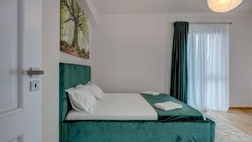 A bedroom with a bed, a painting, a window with curtains, and a door.