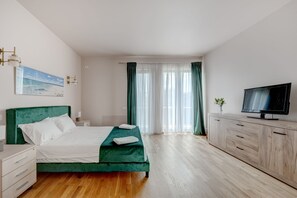 Un dormitorio con cama, televisor, armario y ventana con cortinas.