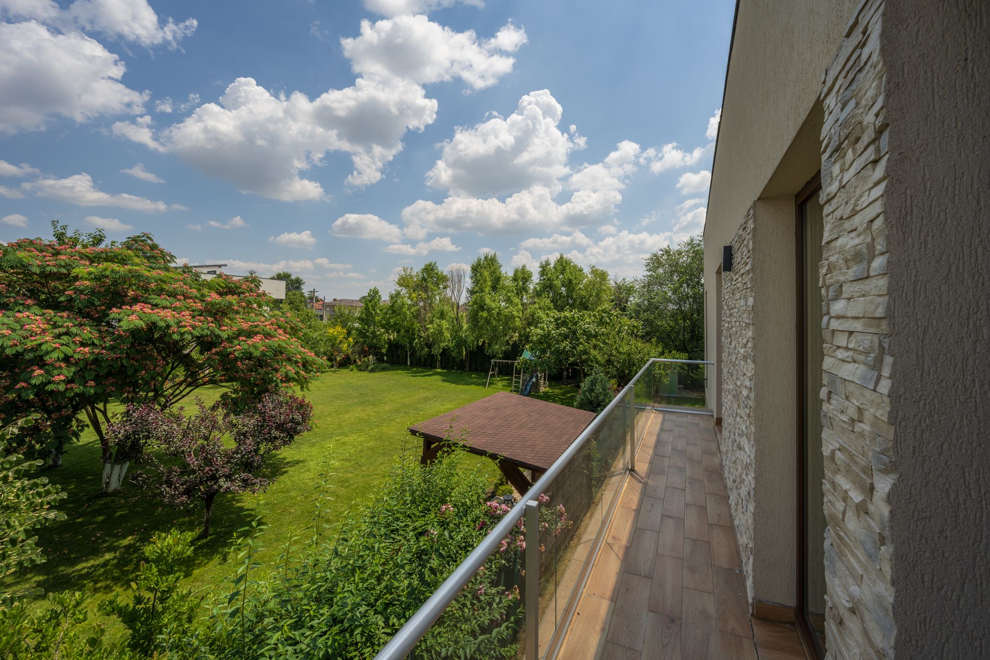 A balcony with a view of a well-maintained garden and a clear sky.