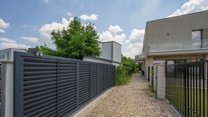 En asfalteret sti der fører til en moderne bygning med et metalhegn på den ene side og en låge på den anden.