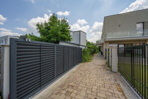 En asfalterad gångväg leder fram till en modern byggnad med ett staket av metall på ena sidan och en grindad entré på den andra.