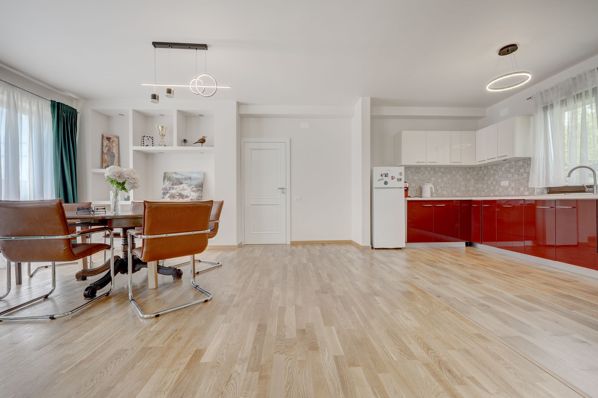 A modern kitchen with red cabinets, a white refrigerator, and a wooden floor.