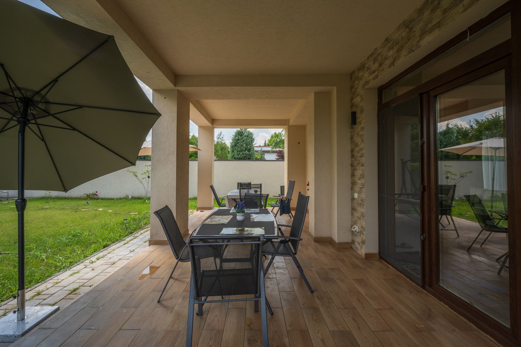 An outdoor patio with a table and chairs, a large umbrella, and a view of the garden.