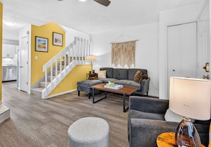 Sala de estar moderna com escada, sofá cinza, mesa de centro e abajur.