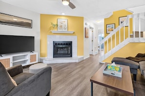 A modern living room with a fireplace, a flat-screen TV, and a staircase leading to another level. - 2BD Townhome Retreat - Close to Downtown & Hiking (Colorado Springs)