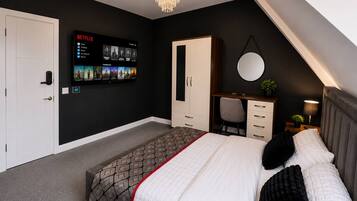 Un dormitorio con cama, escritorio, armario, televisor montado en la pared y candelabro.