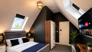 Ein modernes Schlafzimmer mit Dachfenster, einem Bett mit gesteppter Bettdecke, einem Schreibtisch mit Computer und einem Fernseher, der Streaming-Dienste anzeigt.