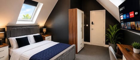 Un dormitorio moderno con tragaluz, una cama con edredón acolchado, un escritorio con computadora y un televisor mostrando servicios de transmisión.