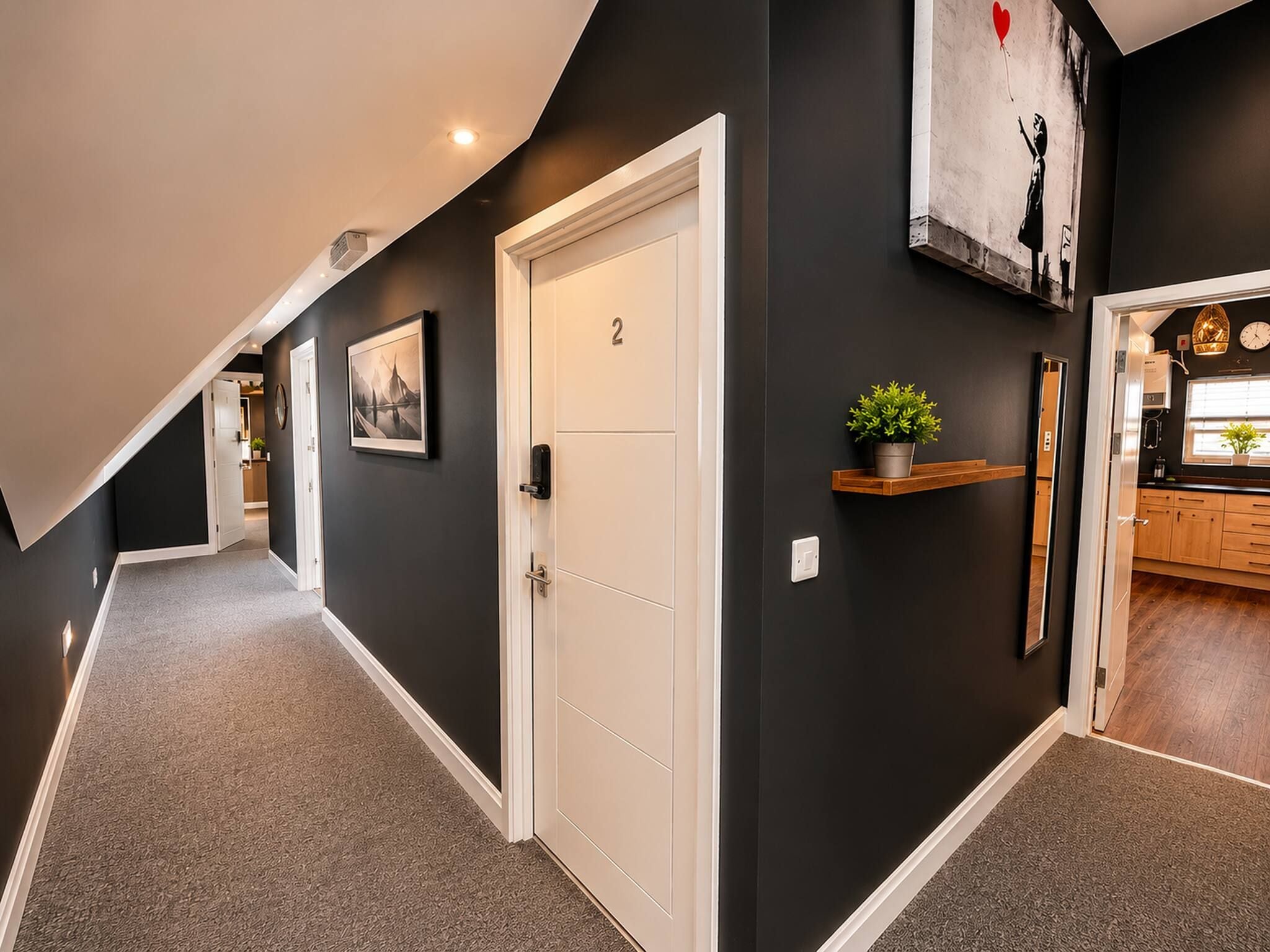A hallway with a white door marked '2', a small shelf with a plant, and a framed picture on the wall.