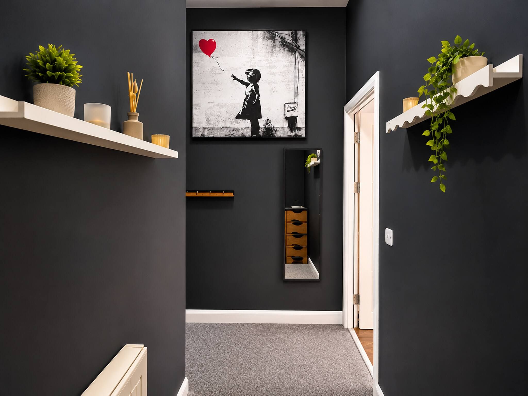 A hallway with a black and white artwork, a mirror, a plant, and a shelf with decorative items.