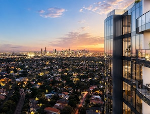 Um edifício alto com fachada de vidro moderna, com vista para uma área urbana densamente povoada, com ruas e edifícios residenciais visíveis.