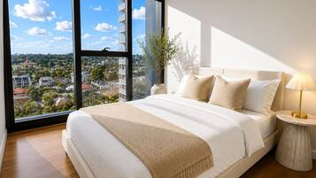 Un dormitorio con un ventanal grande, una cama con ropa de cama blanca, una mesita de noche con una lámpara y una planta.