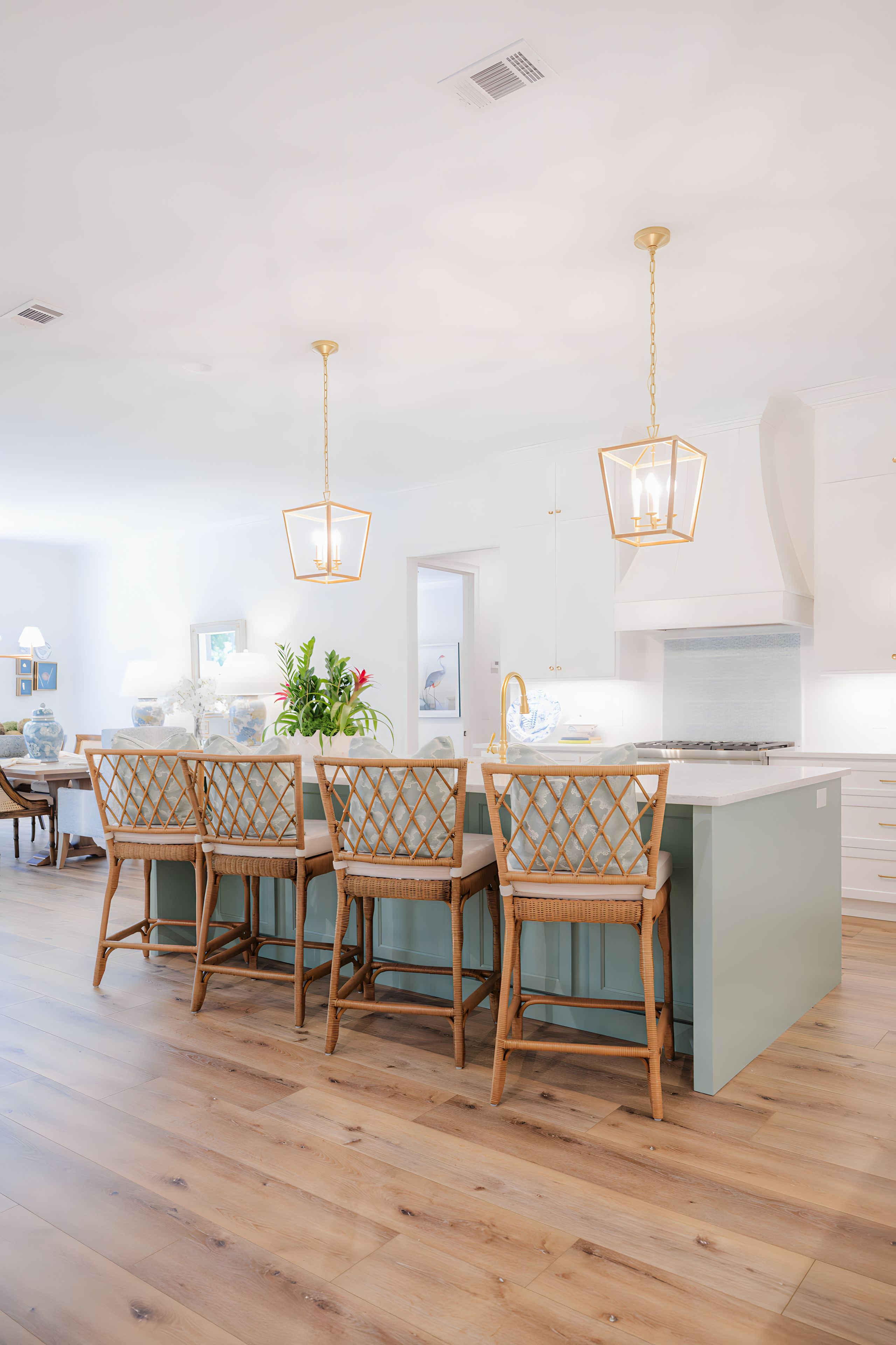 A spacious kitchen with a central island, wicker chairs, pendant lighting, and a view into the dining area.