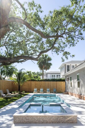 A swimming pool with a wooden deck, surrounded by a wooden fence, and a large tree overhead. - East Beach Retreat sleeps 12 with a pool (St. Simons Island)