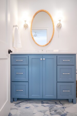 A bathroom with a blue vanity, a round mirror, and a white sink. - East Beach Retreat sleeps 12 with a pool (St. Simons Island)