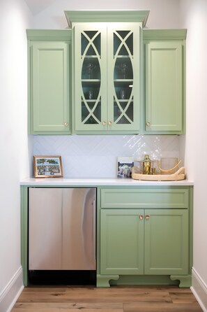 A kitchen with green cabinets, a white countertop, and a stainless steel refrigerator. - East Beach Retreat sleeps 12 with a pool (St. Simons Island)
