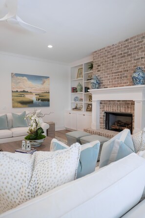 A living room with a white sofa, a fireplace, and a large landscape painting. - East Beach Retreat sleeps 12 with a pool (St. Simons Island)