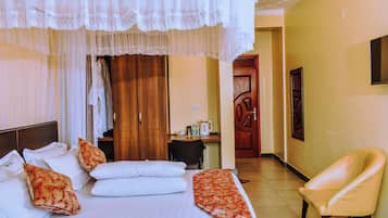 A hotel room with a bed, a chair, a wardrobe, and a desk with a coffee maker.