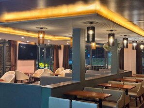 L'intérieur d'un restaurant avec des banquettes, des tables et des lampes suspendues.