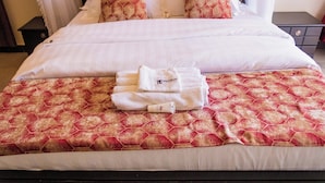 Una cama bien hecha con un edredón estampado, una toalla blanca doblada y un tubo de crema hidratante.