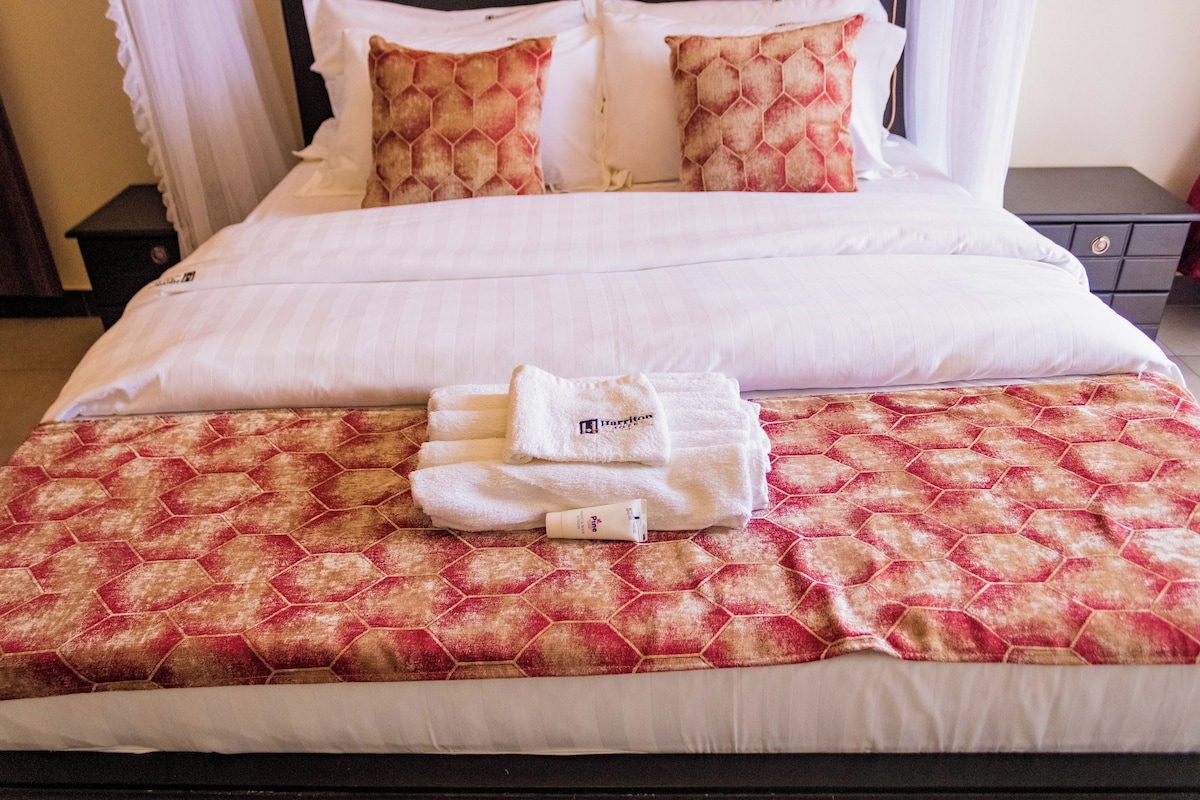 Un lit bien fait, avec une couvre-lit à motifs, une serviette blanche pliée et un tube de lotion.