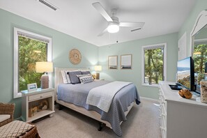 Ein Schlafzimmer mit einem Bett, Nachttischen, einem Deckenventilator und großen Fenstern.