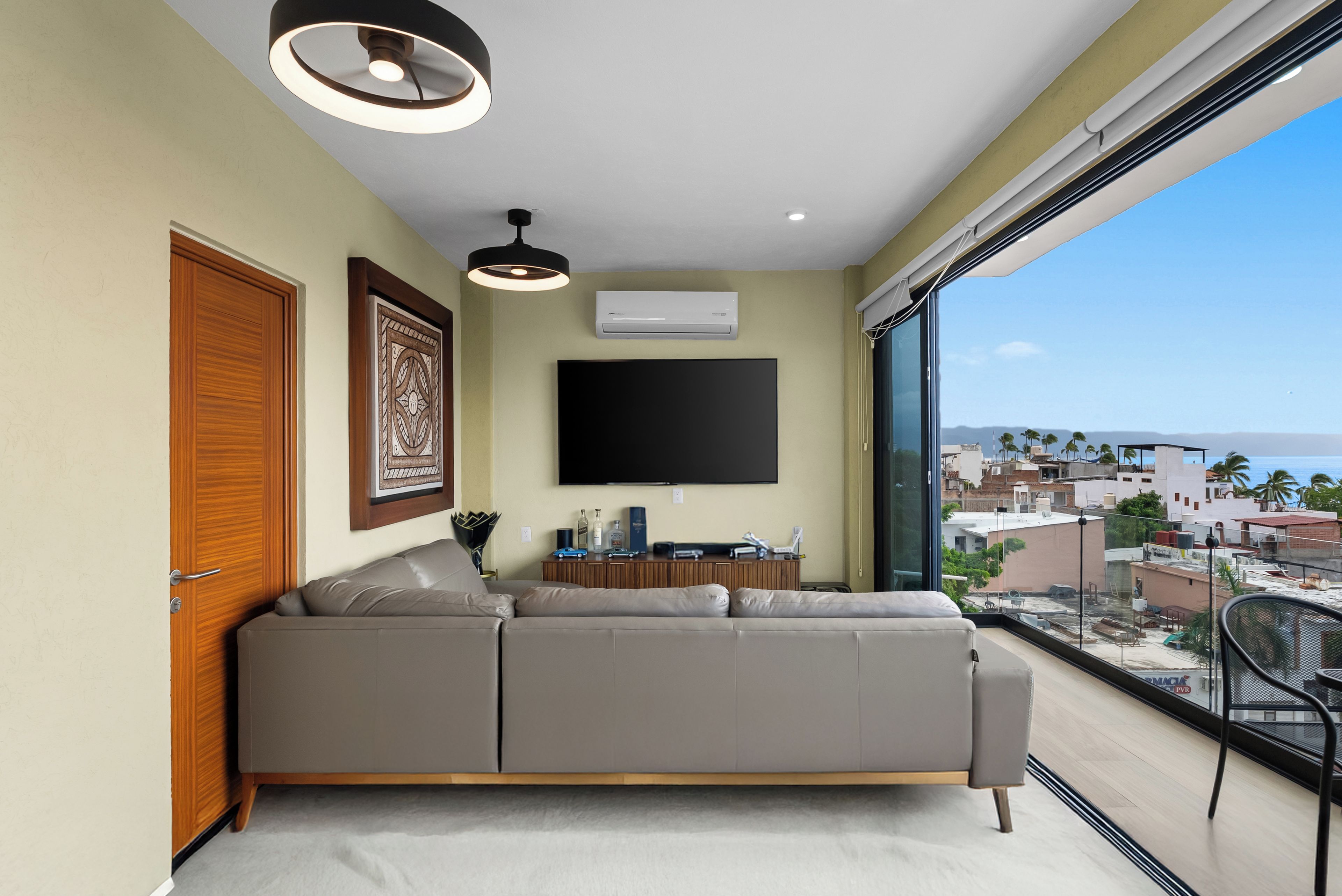 Una sala de estar moderna con un sofá grande, un televisor de pantalla plana y un balcón con vista a la ciudad.