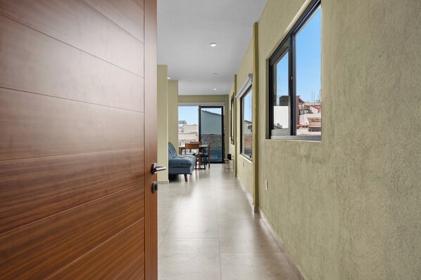 Un pasillo con puerta de madera, un comedor con sillas y mesa, y ventanas amplias.